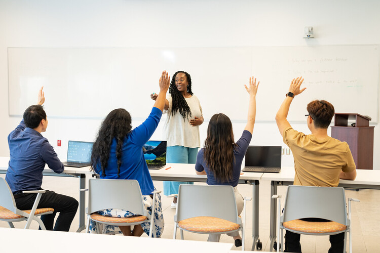 A group of students and a teacher in a classroom, with the students raising their hands